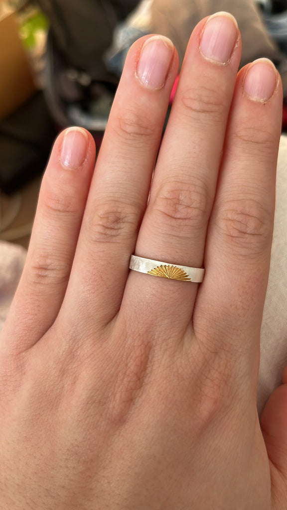 Slim silver ring with gold sunrise being worn on the middle finger of a woman's hand