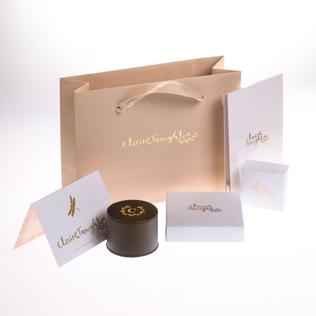 Jewellery gift packaging for Claire Troughton Jewellery. A beige gift bag is at the back with white and black jewellery boxes in front all printed with a gold Claire Troughton logo
