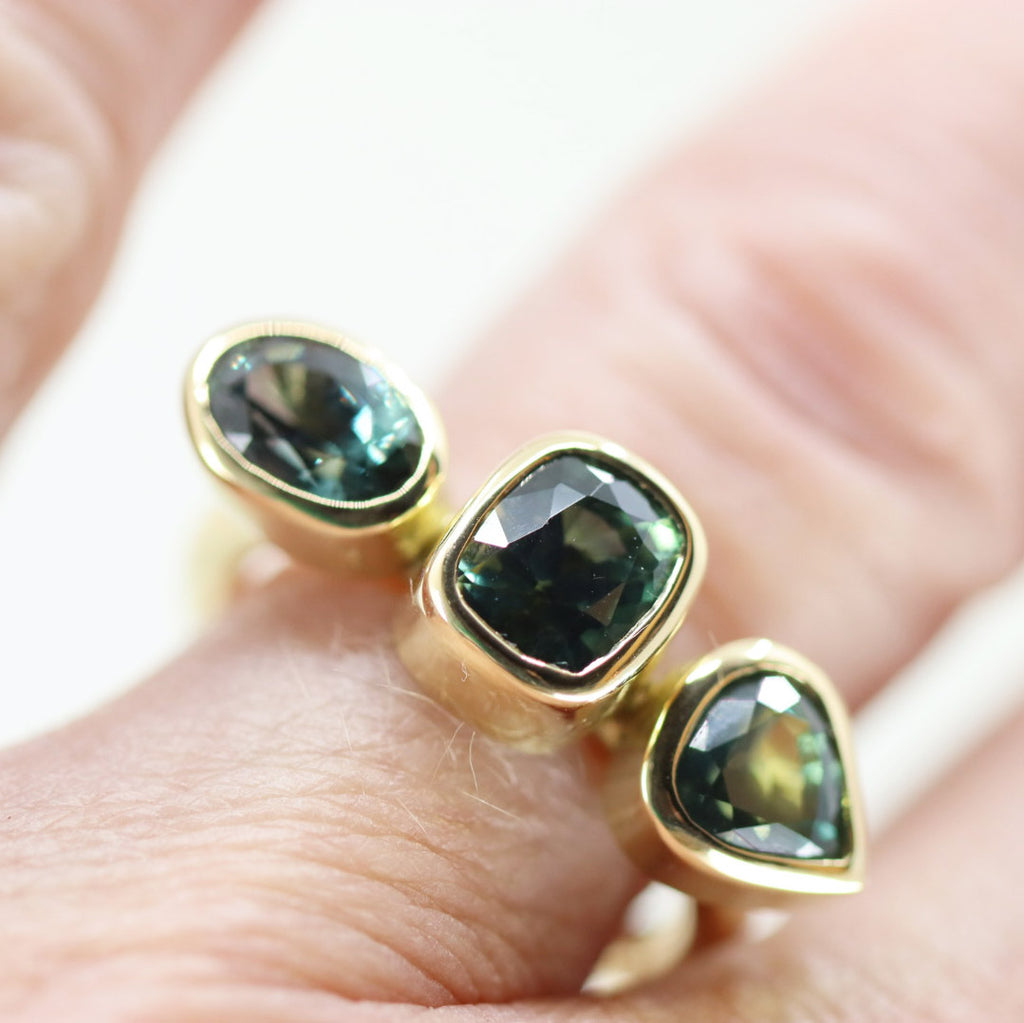 Large oval, cushion and trillion cut green sapphire ring on a finger