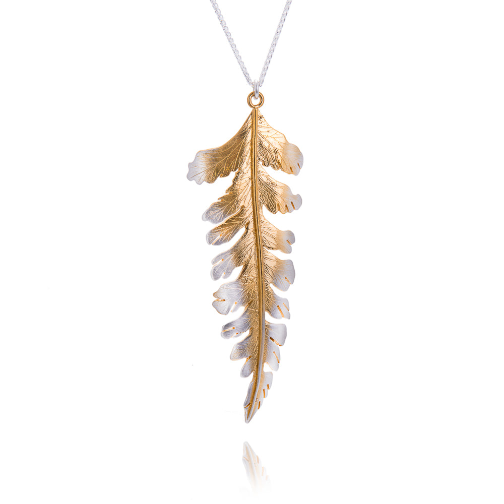A large fern shaped pendant with gold down the centre fading to silver at the tips. The pendant hangs on a silver chain