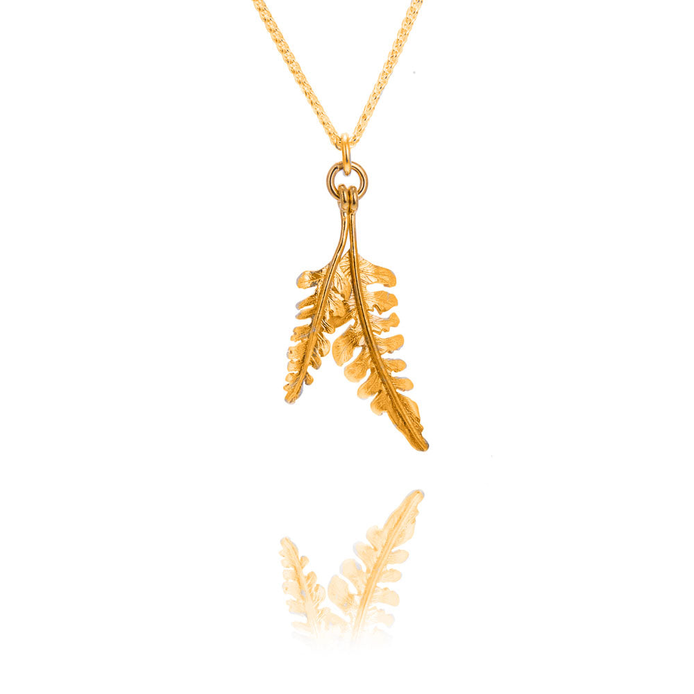 A tiny and small fern shaped pendant in gold on a gold chain