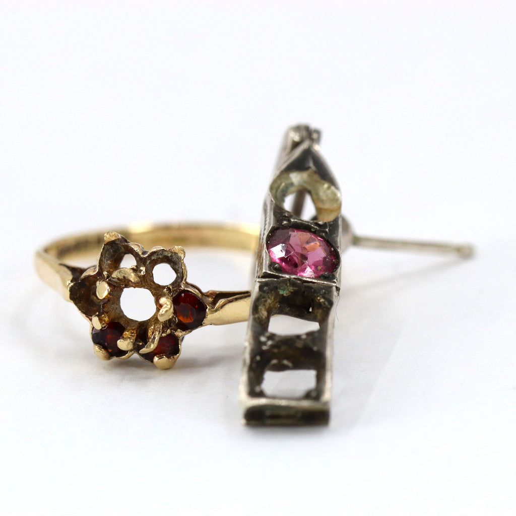 A gold cluster ring with 3 garnets and 4 empty settings. A silver earring with one pink tourmaline and several missing stones lies on top