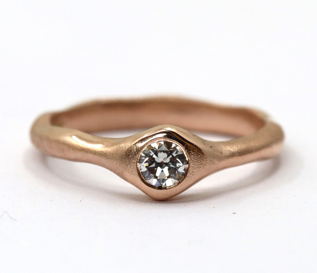 Red gold wavey ring with a round diamond set flush with the surface of the metal. The front of the ring widens out to accomodate the diamond