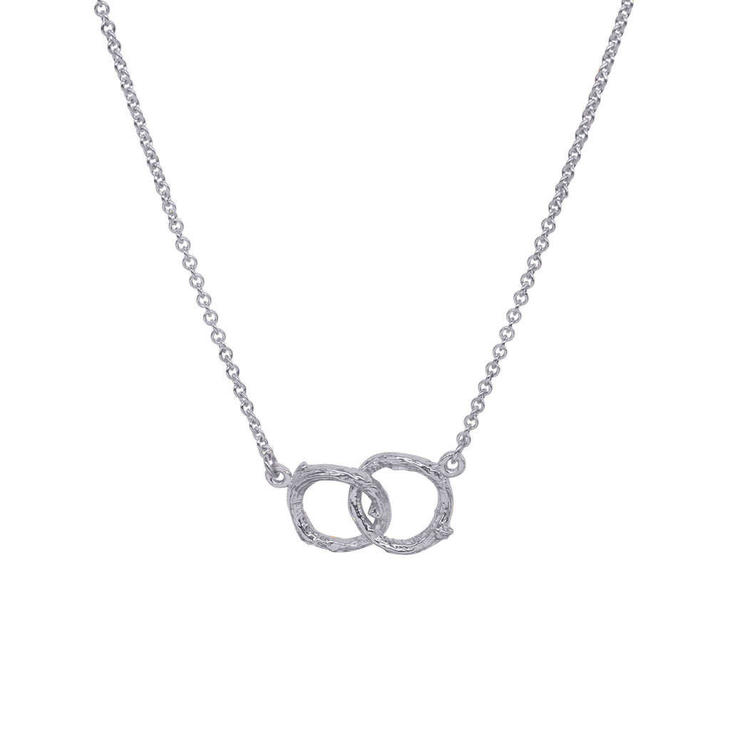 Two interlinked small silver circles with a twig texture hang from a silver necklace