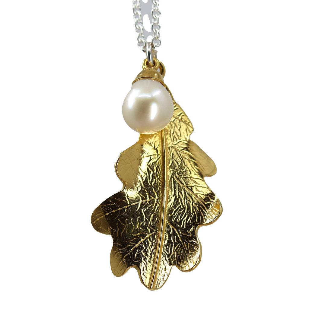 A large gold oak leaf pendant with engraved vein pattern and a white pearl pendant, both hanging on the same silver chain