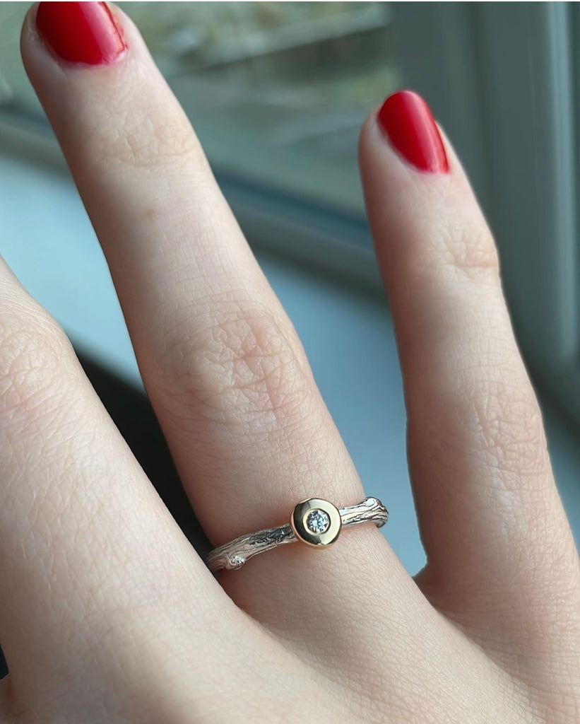 Silver twig ring with gold bud worn on the ring finger of  hand with red nails