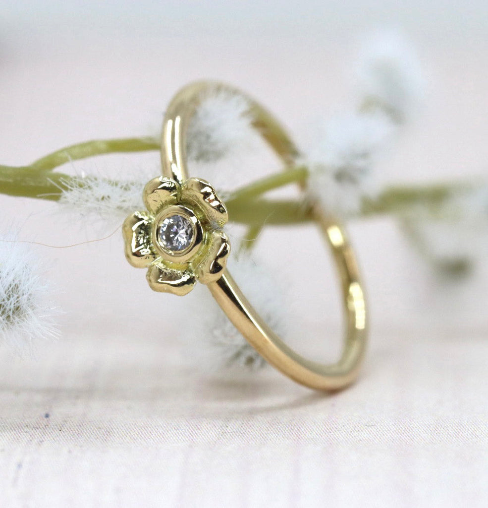 a yellow gold flower ring set with diamond, leaning against a plant stem
