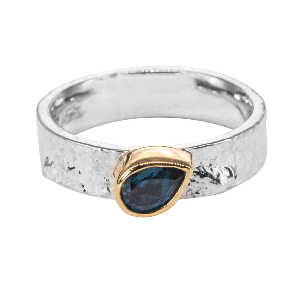 Silver ring with pear blue topaz sat diagonally across the ring, encased in gold