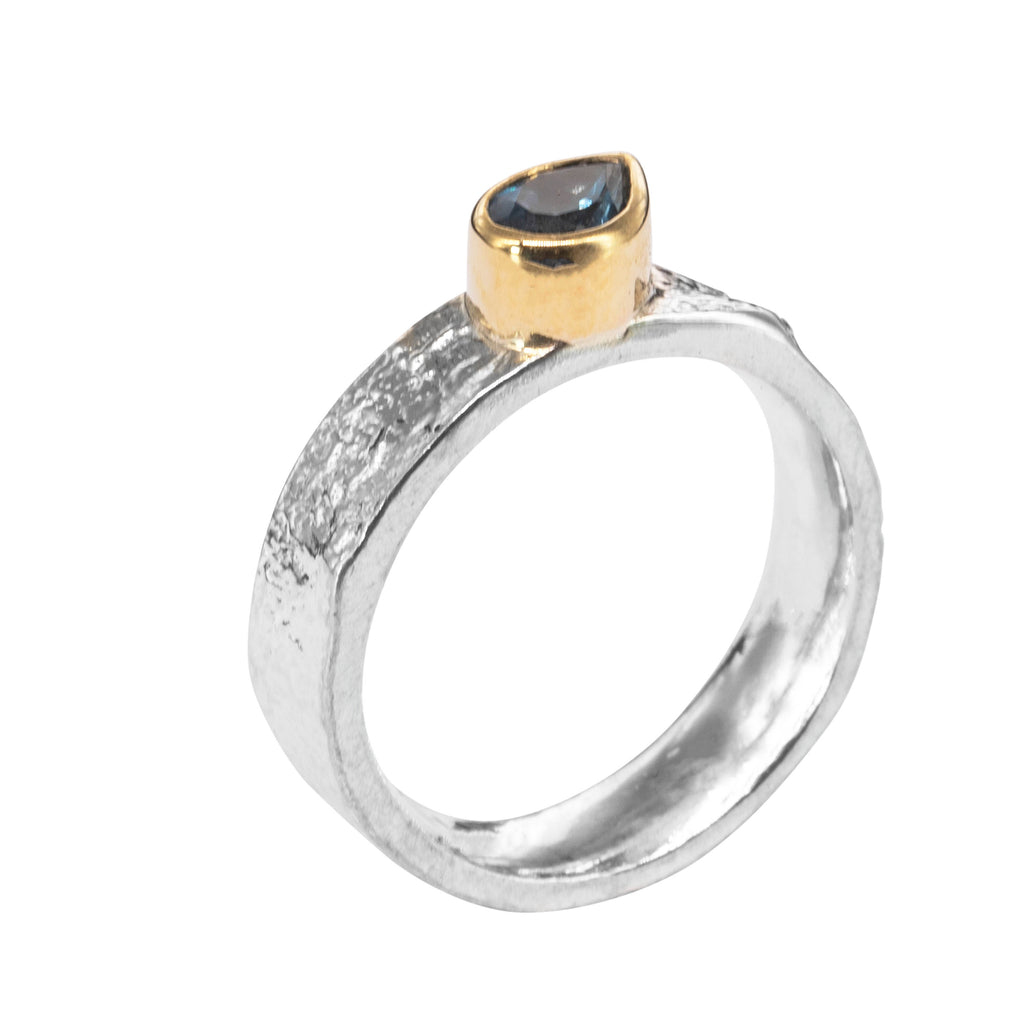 side view of a silver ring with a tall smooth setting in gold holding a blue pear shaped stone