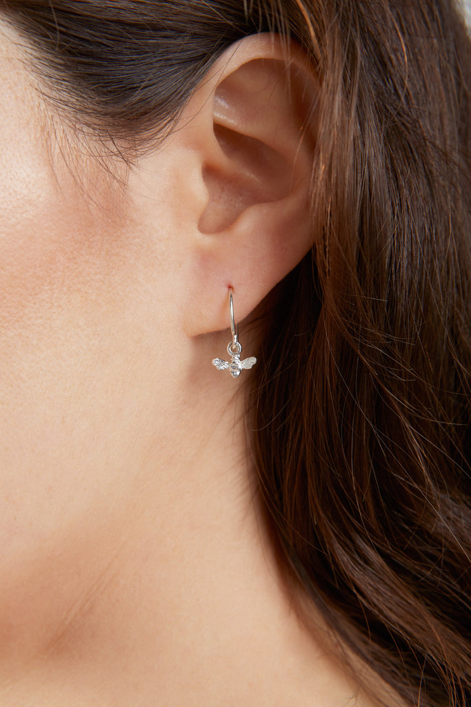 Tiny silver bee hook earrings on earlobe