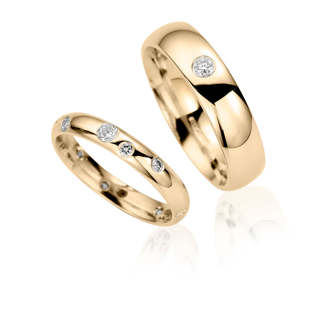 slim yellow gold wedding ring set with several diamonds alongside a wider yellow gold ring flush set with one diamond