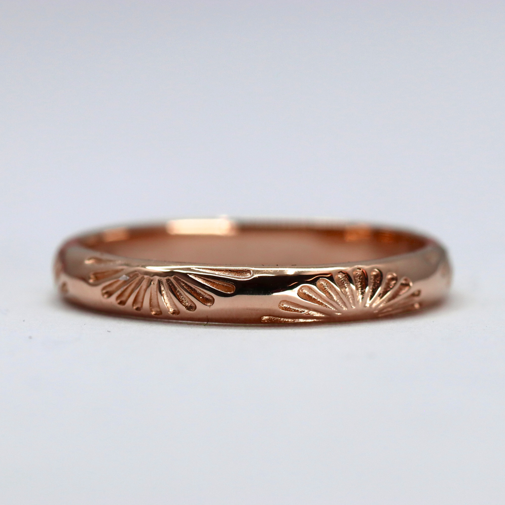 Rose gold ring with intricate design on a light gray background