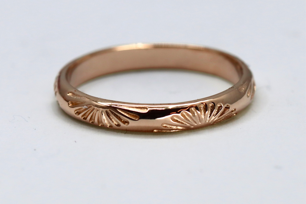 Rose gold ring with sunshine design on a light gray background
