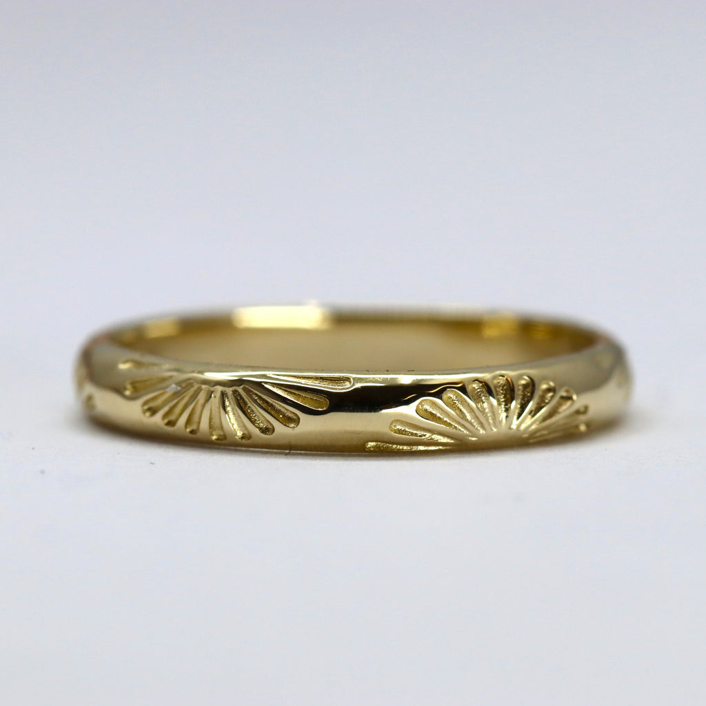 Gold ring with sunburst pattern on a light grey background