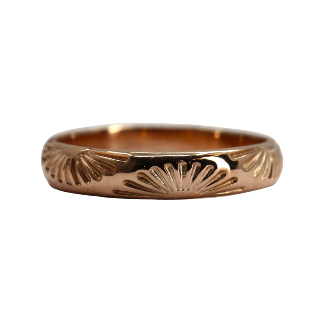 Rose gold ring with decorative sun pattern on a white background