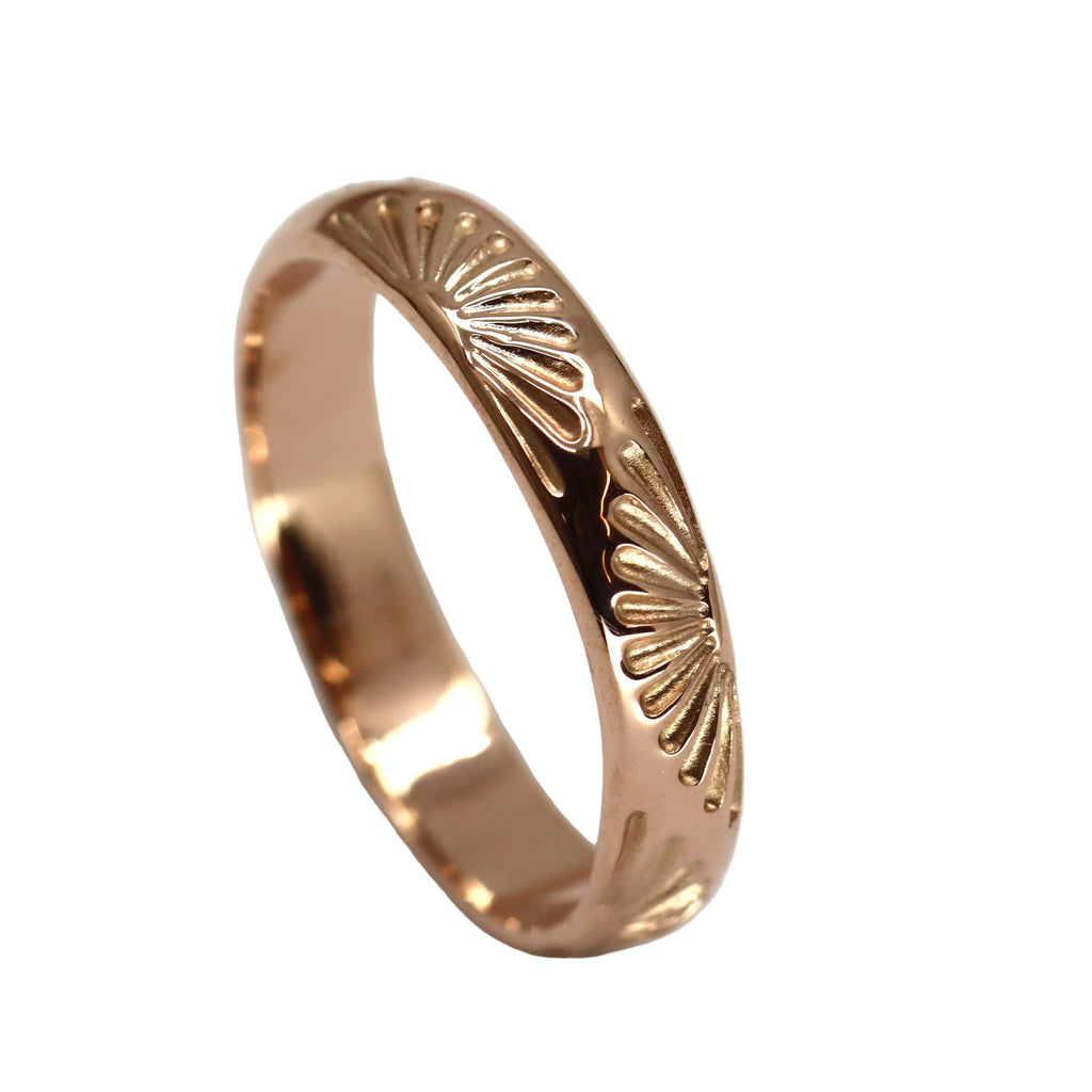Rose gold ring with sunburst pattern on a white background
