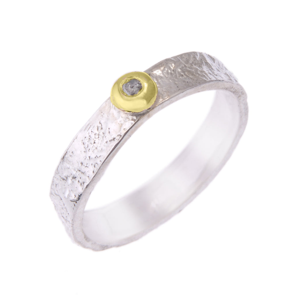 Silver ring standing on end. The outside of the ring has a textured surface. There is a pebble of yellow gold on the top with a grey diamond set into it