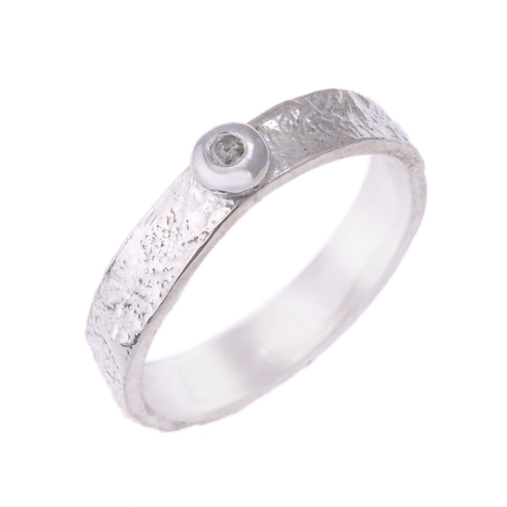 5mm wide silver bark textured ring standing on end. There is a round silver pebble on the top, which is almost as wide as the ring. The pebble has a speckled grey diamond set into it.