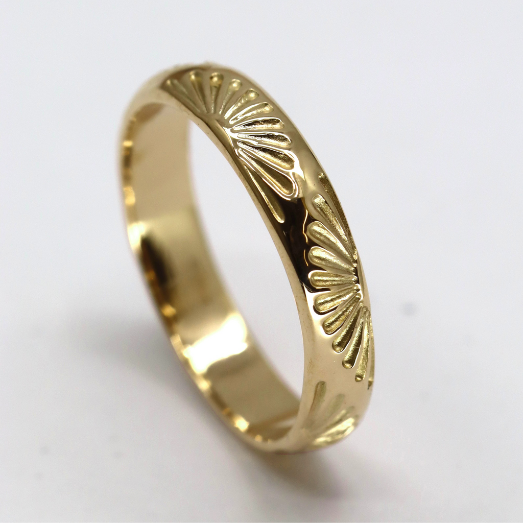 Yellow gold wedding ring with a sun engraving on a light grey background