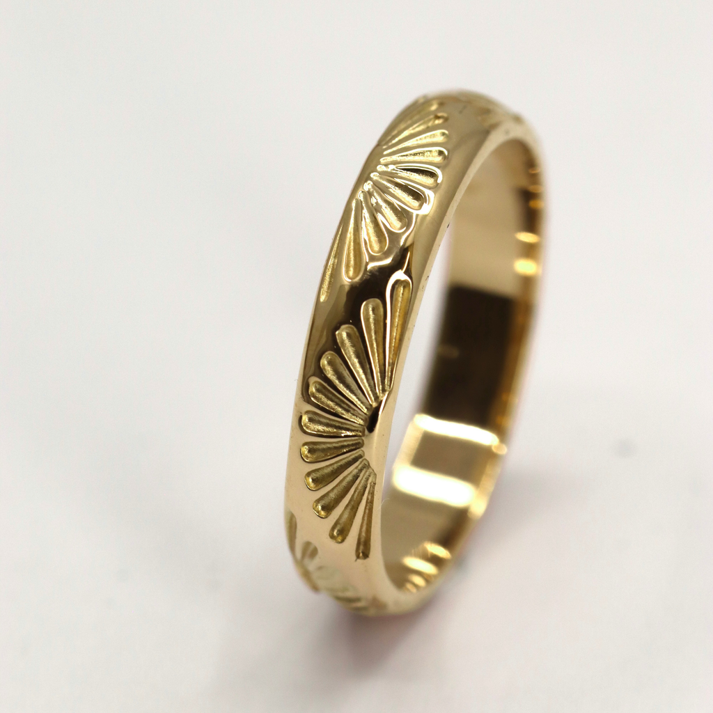 Gold ring with sunburst pattern on a light gray background