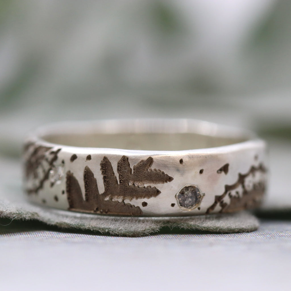 Silver ring with an engraved fern design on a soft surface