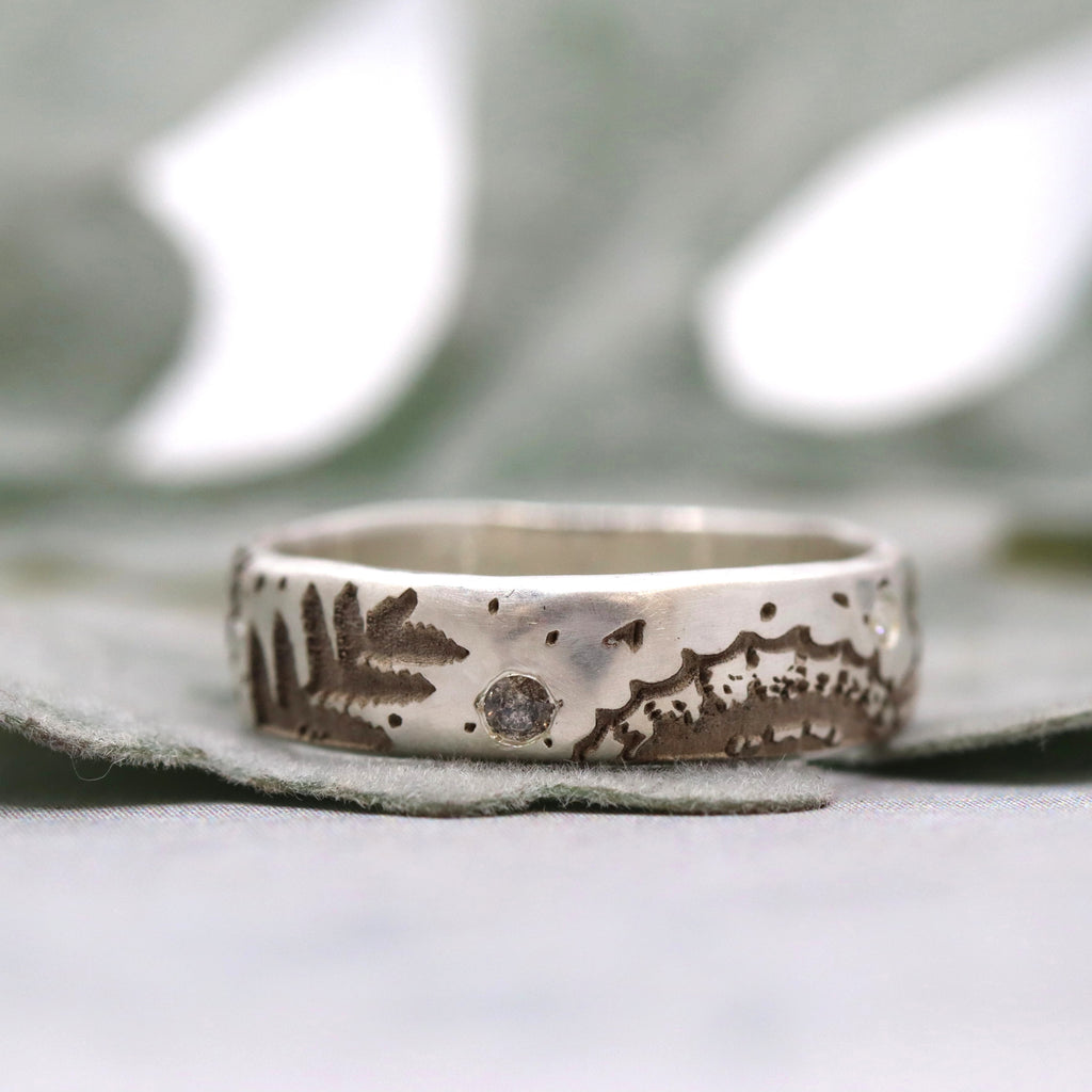 Silver ring with an engraved fossil pattern and small diamond on a neutral background