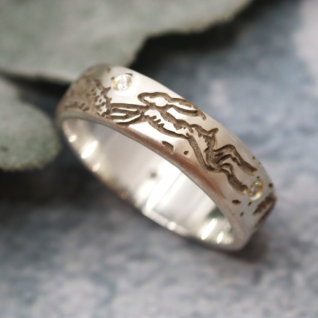 Silver ring with an engraved leaping hare design on a stone surface