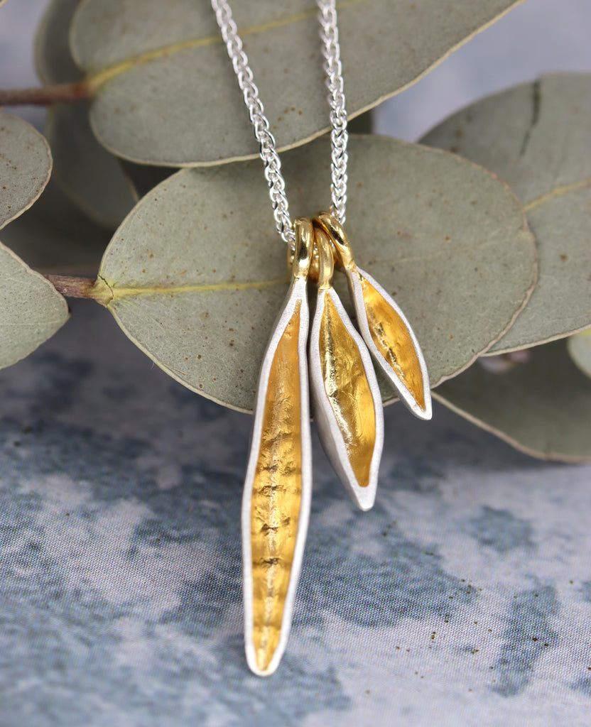 Necklace with 3 gold and silver leaf pendants on a leafy background