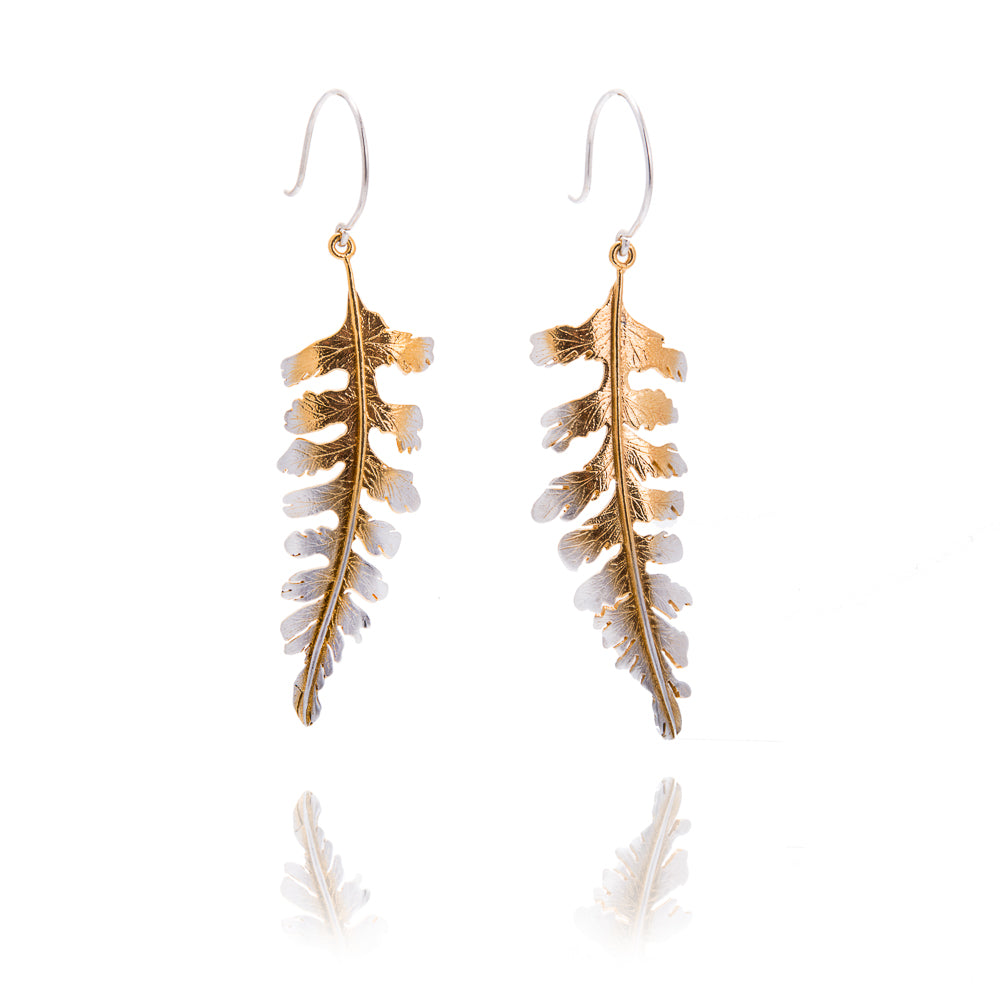 Large fern shaped earrings in gold with silver on the tips. The earrings hang from silver hook wires