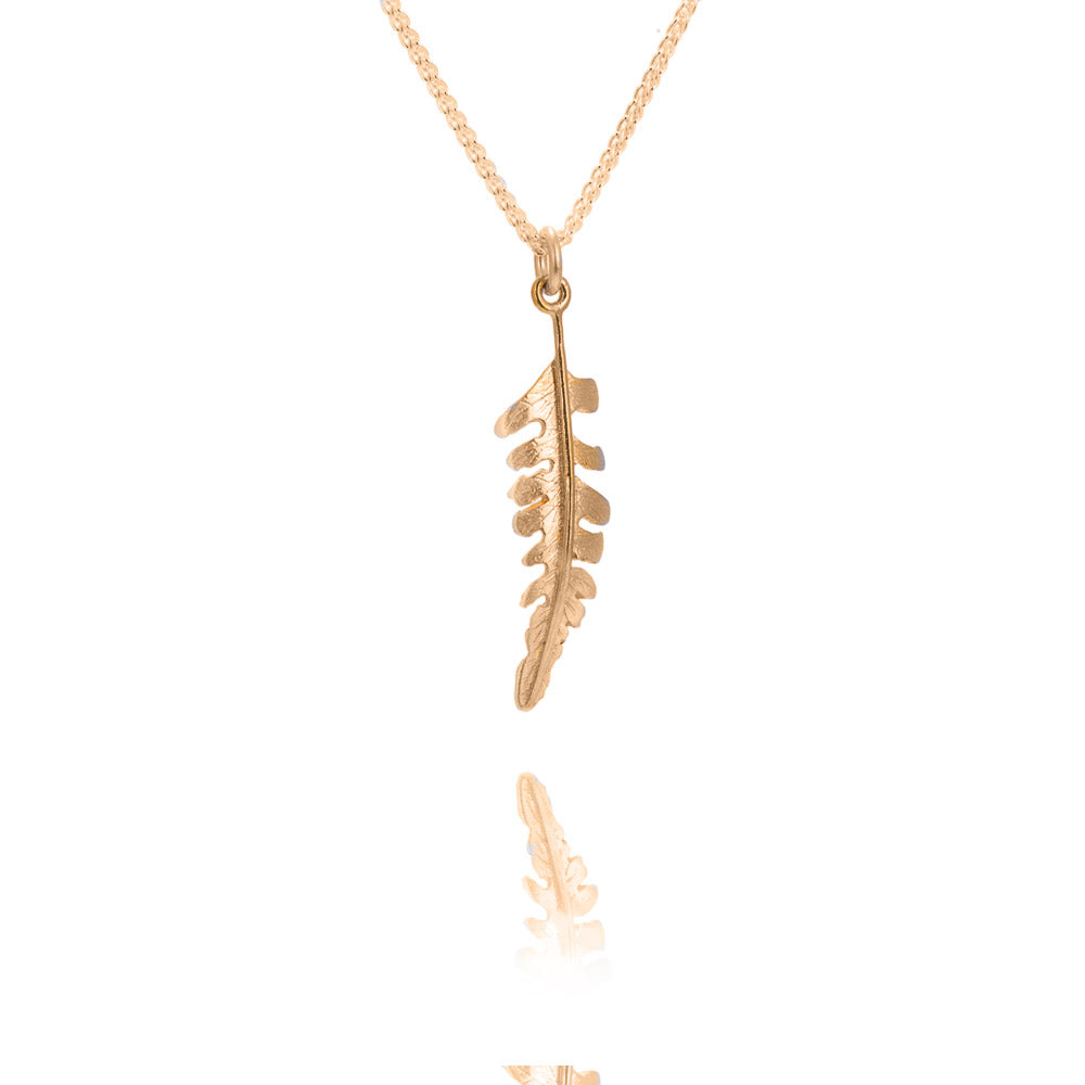 A small gold fern shaped pendant on a gold chain. There is a reflection of the fern underneath