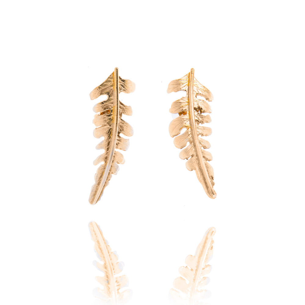 A pair of gold fern shaped stud earrings. The ferns curve away from each other. There is a reflection of the fern tips underneath