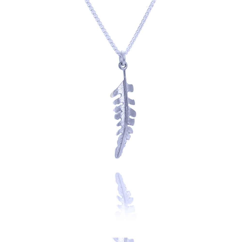 A small fern shaped silver pendant hanging from a silver chain. There is a reflection of the pendant underneath it.