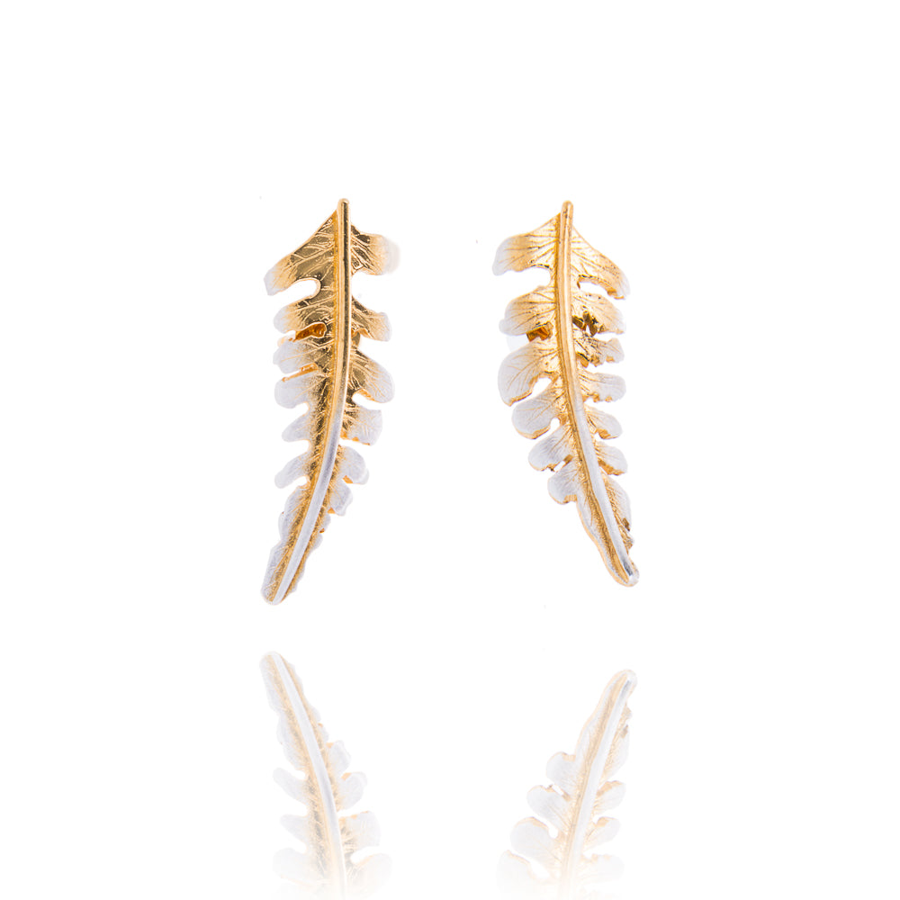 A pair of small fern shaped stud earrings with gold down the centre and silver edges. The ferns curve away from each other. There is a reflection of the earrings underneath