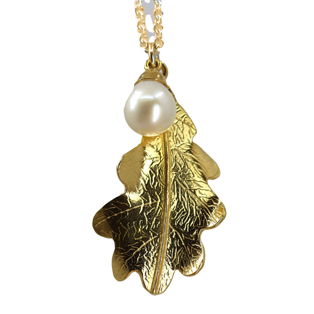A large gold oak leaf shaped pendant with engraved vein pattern and a white pearl hanging from a gold linked chain