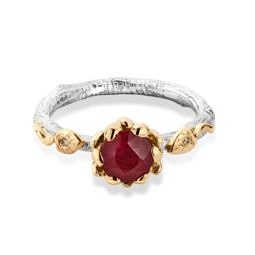 White gold engagement ring with ruby at the front, surrounded by gold petals. There are 2 leaf shapes at each side of the ruby.