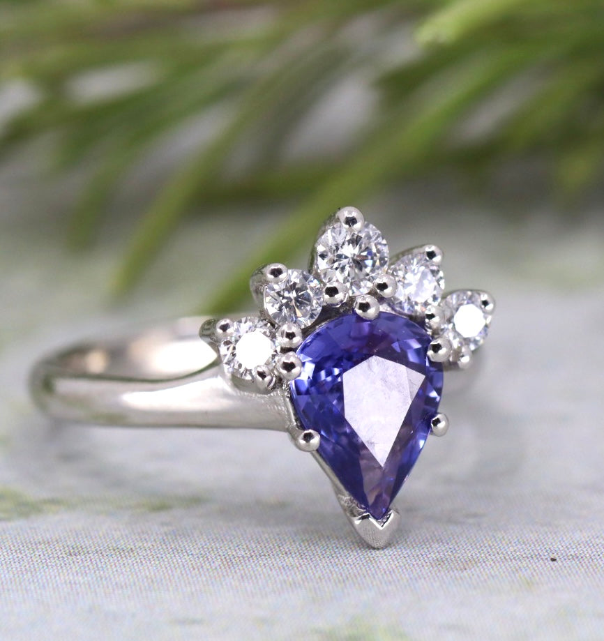 Platinum engagement ring with pear shaped purple sapphire with diamonds around the curved part of the stone