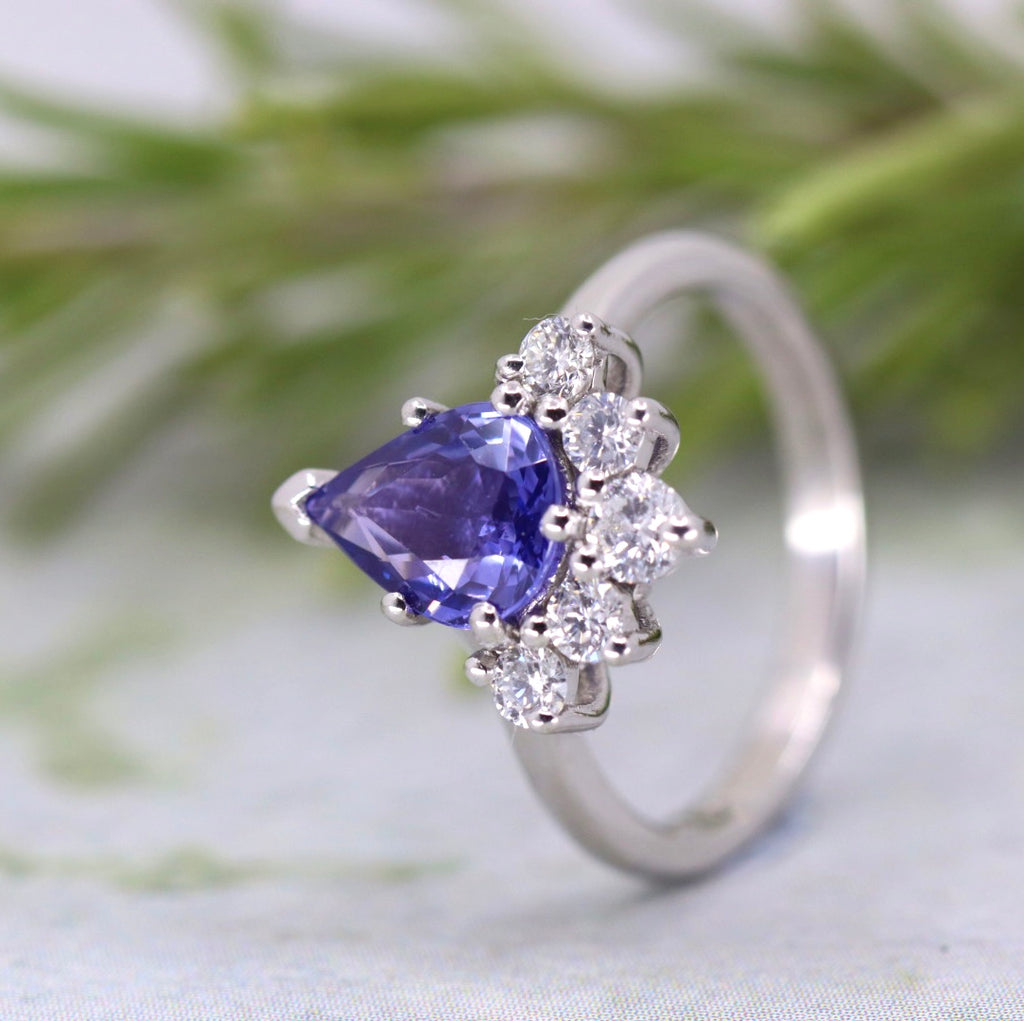 White metal ring with a large purple pear shaped sapphire with diamonds around the bottom