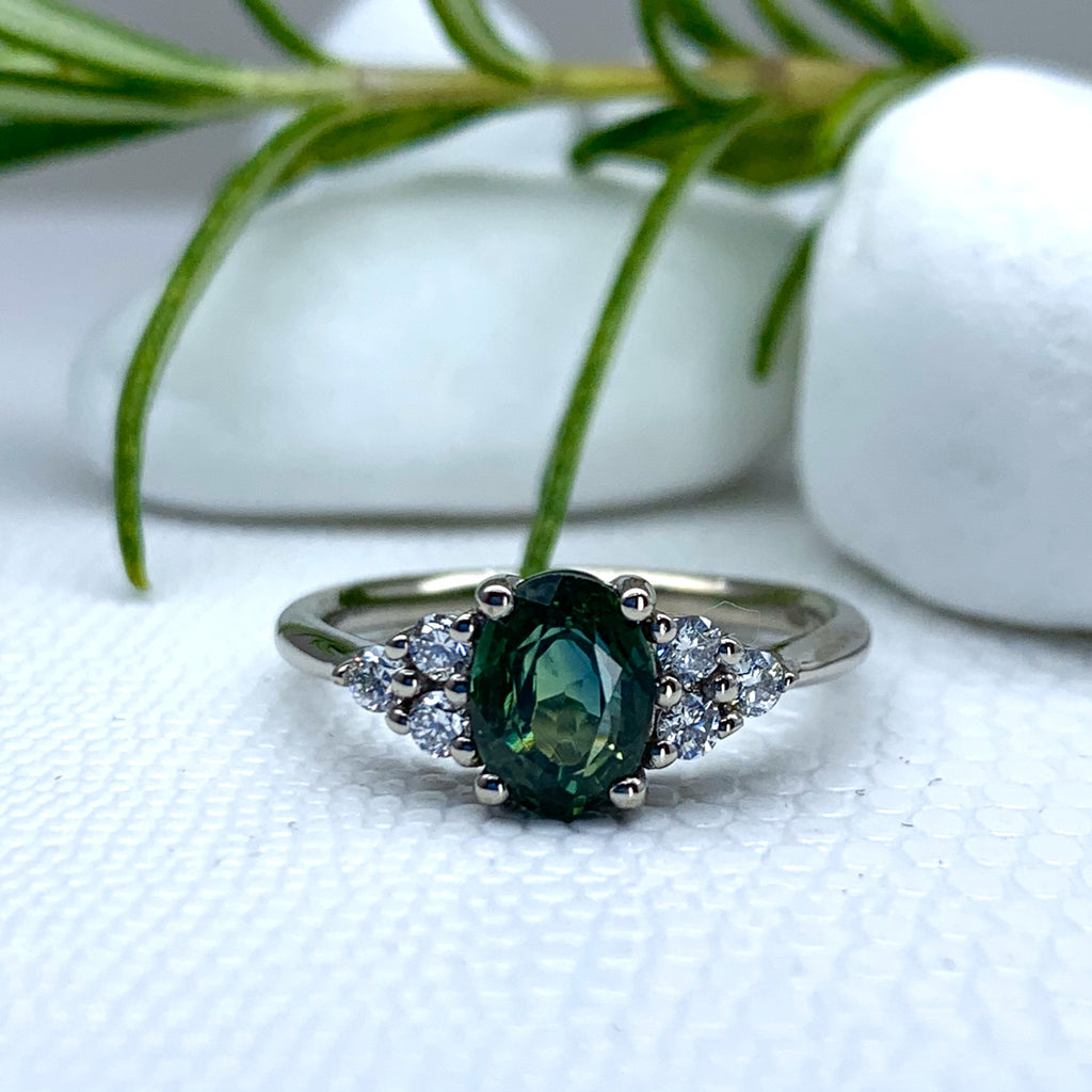 A large oval teal green gemstone set in a white gold ring . The green stone has 3 white stones in a triangle formation on either side of it