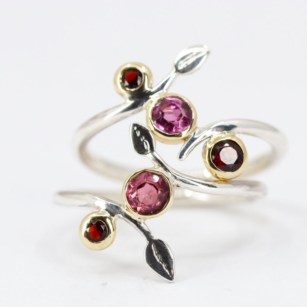 Two twisting wire silver rings stacked on top of each other. The wires have leaf shapes on each end. Pink and red stones in gold settings between the silver wires