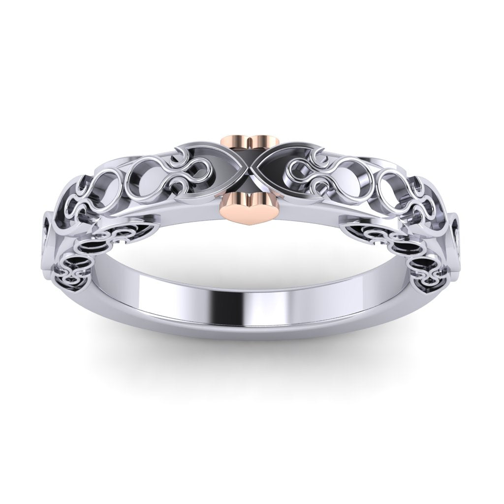 A platinum wedding band viewed from the top. It has an intricate spade and circle design standing up from the band and a rose gold heart on each side