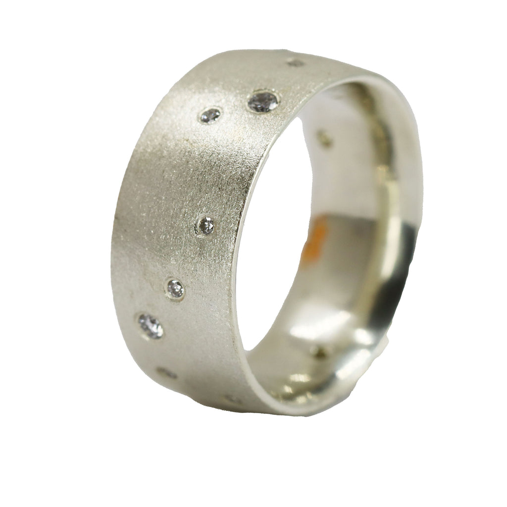 Wide silver ring standing on end. The surface is matt and studded with several flush set diamonds
