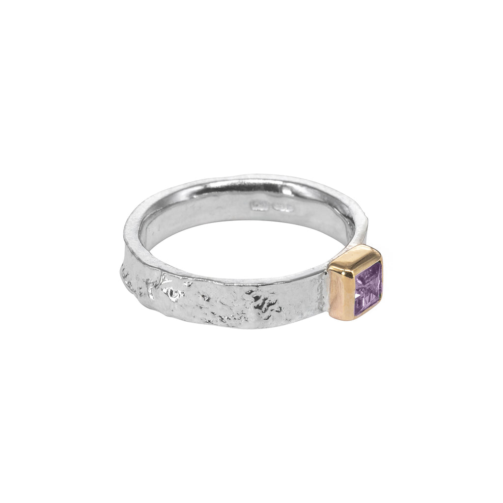 side view of silver ring with gold setting sticking out on right side, holding a purple amethyst
