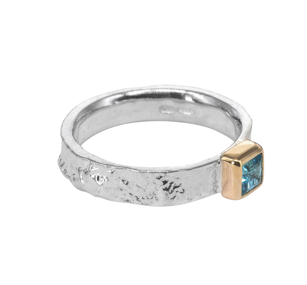 Textured silver ring from side with gold square setting holding blue stone to the right side