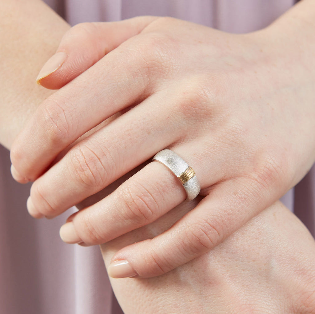 A woman's hand wearing a silver ring with 5 gold wires running across the width of it.