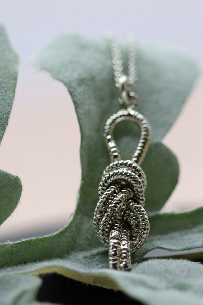 a white gold pendant made to look like a knot used in indoor rock climbing, sitting on a leaf