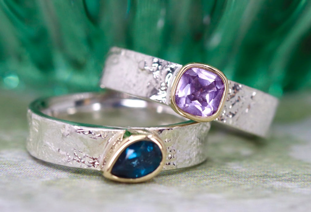 2 silver textured rings with green background. 1 ring has a cushion amethyst and 1 has a pear blue topaz