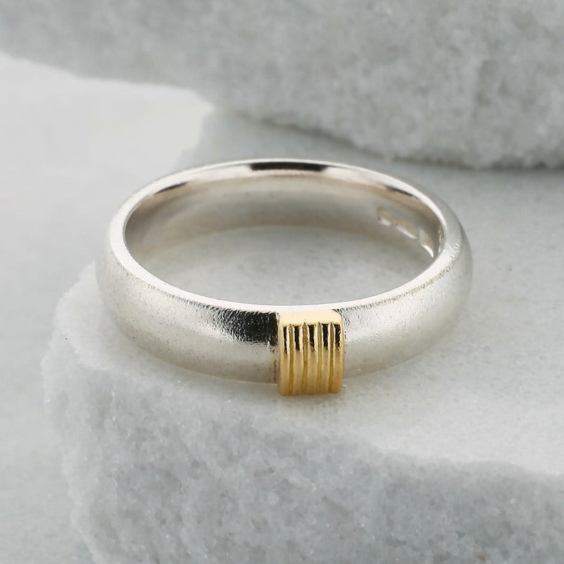 4mm wide silver court section ring lying on a white stone. The ring has 5 gold wires on the front
