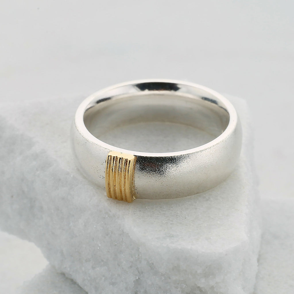 Wide silver ring on a white rock. The ring has 5 gold wires running across it and is matt outside and polished inside