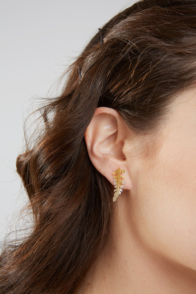 Woman's ear lobe with a fern shaped stud earring hanging down from the lobe