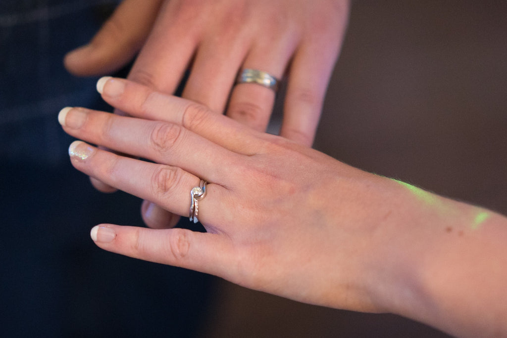 A ladies hand with a twist shank engagement ring and shaped to fit wedding ring placed over a gents hand showing a wedding ring